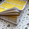 A close-up of an open A5 I Forget Things Memo Pad 2 with yellow and white pages rests on a terrazzo-patterned surface. The slightly fanned pages reveal printed lines and boxes.