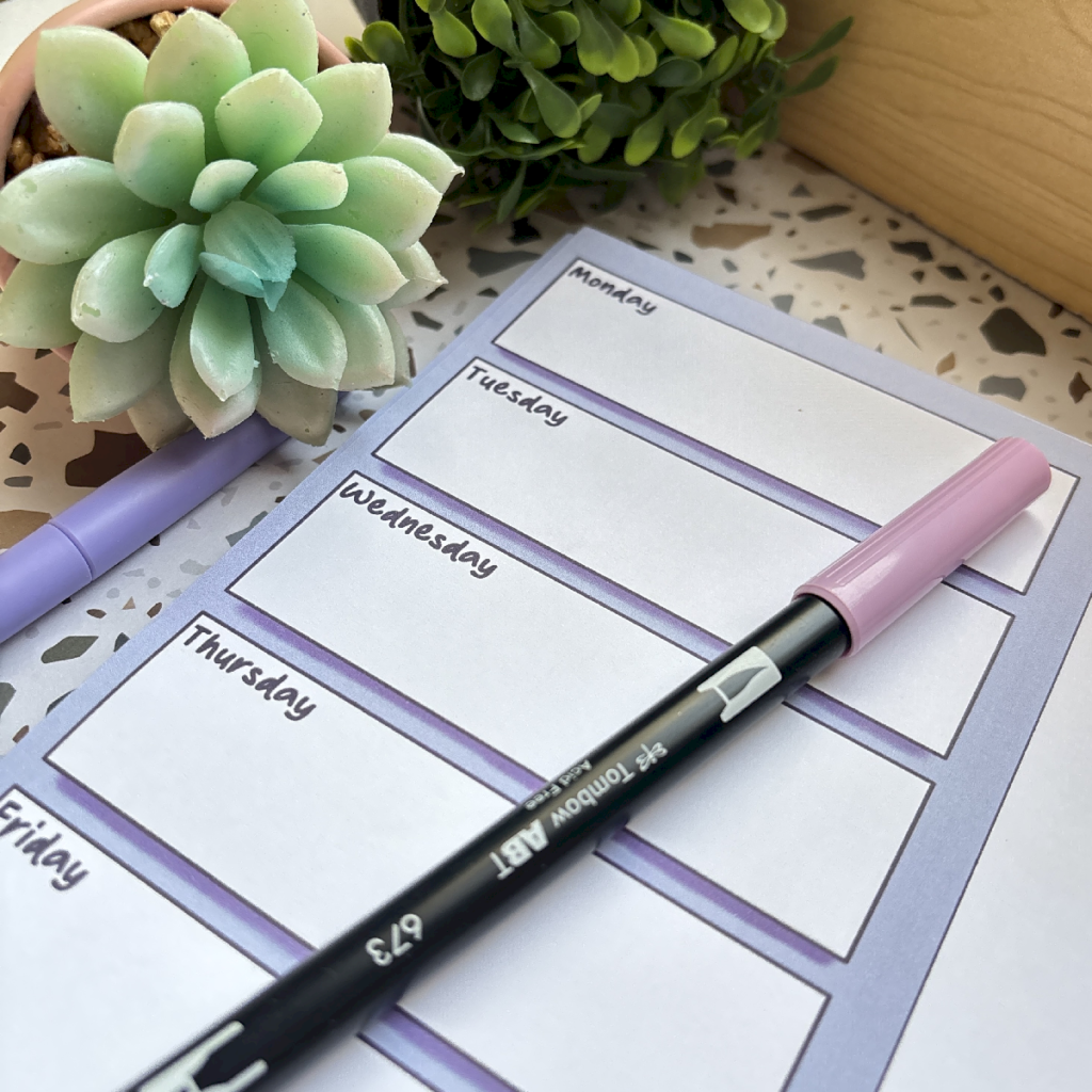 The A5 Weekly Planner Pad 3 with blank weekday sections rests on a terrazzo surface, accompanied by a black pen with a pink cap and a green succulent in a pink pot.