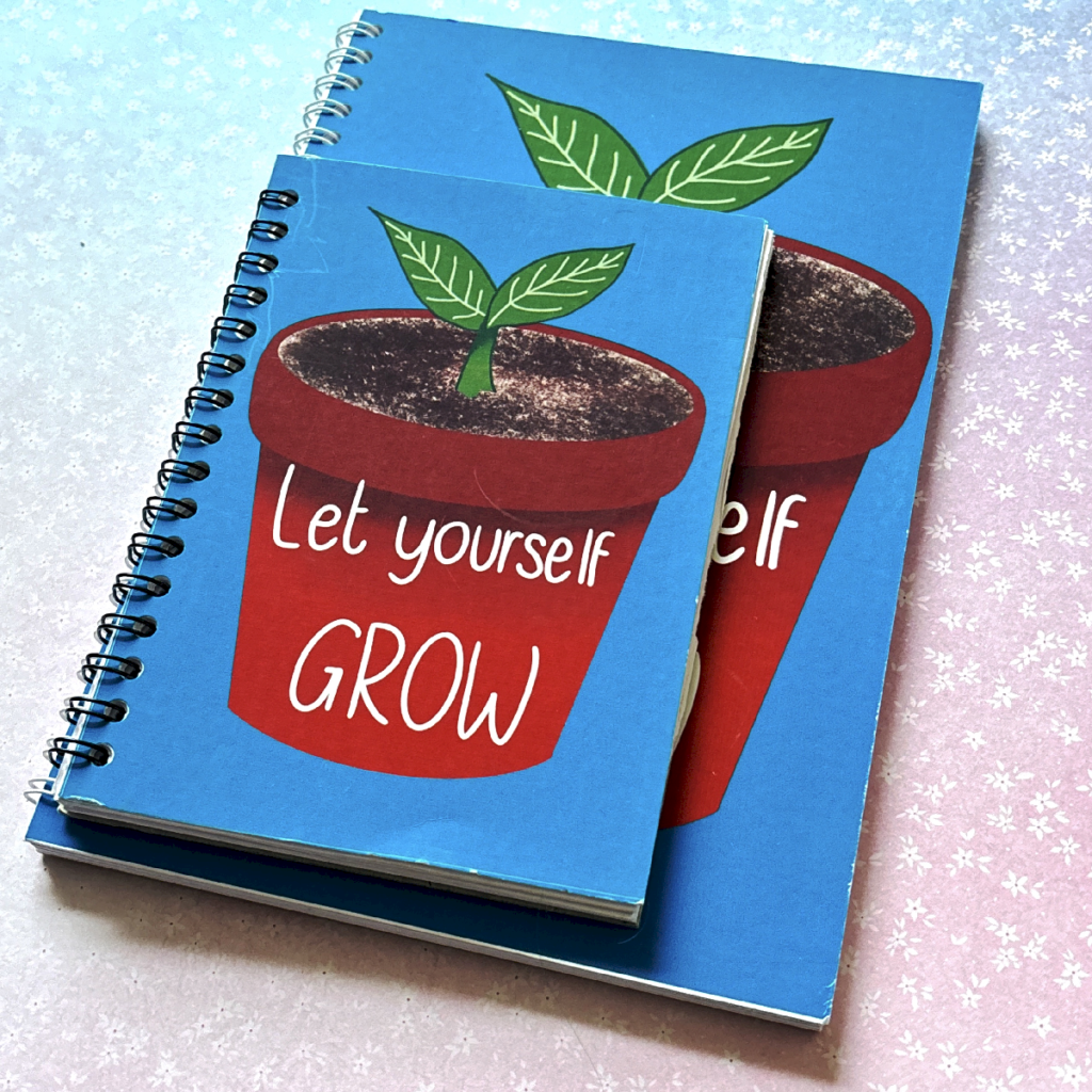 Two spiral bound notebooks lay on a pastel background. The notebooks have the same design, and the one on top is smaller than the bottom one. The notebook has a turquoise cover and a plant pot with a plant sprouting illustration. On the plant pot it says 'let yourself grow'.