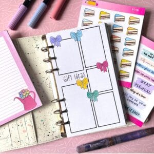 Gift Buying Personal Ring Insert A personal ring planner open on a table. The top sheet shows a 'gift buying' insert. Around the planner are sticker sheets, a pink memo pad and some pens.