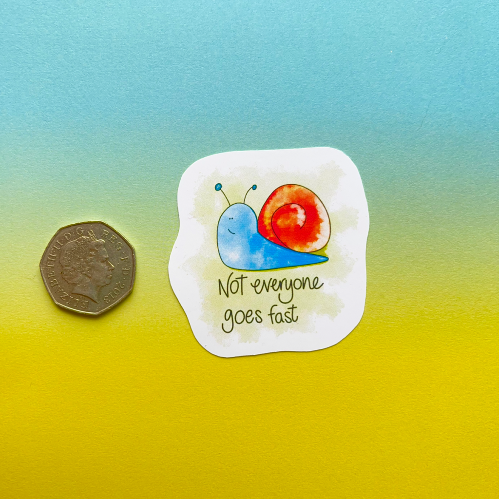A single sticker with a 50p coin next to it for size reference. A snail with a happy face, a bright blue body and orange shell. Under the snail it says 'not everyone goes fast'. The image has a blue to yellow hombre effect background.