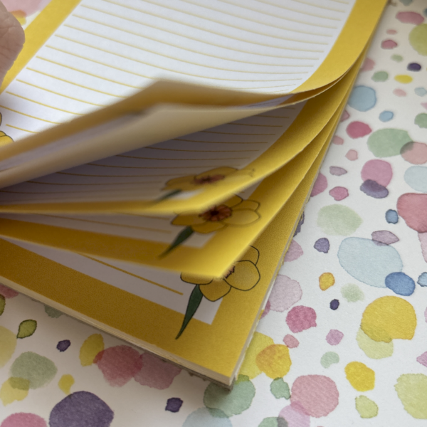 The Daffodil A6 Memo Pad features floral corners on a pastel dotted background; its slightly raised pages reveal lined paper and charming flower designs.