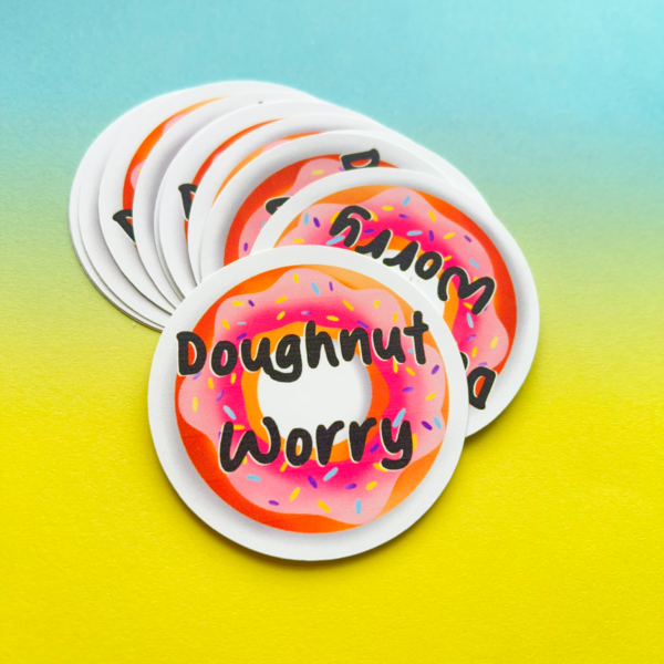 The Doughnut Matt Vinyl Sticker 2 features a pink iced doughnut with sprinkles and “Doughnut Worry” in black letters on a blue and yellow gradient background.