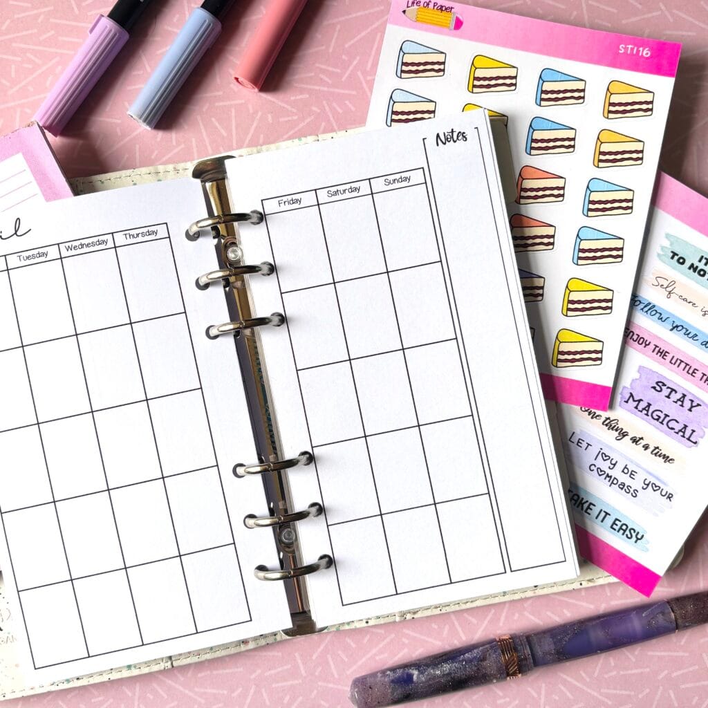 A personal ring planner open on a table. The top sheet shows a 'future log' insert. Around the planner are sticker sheets, a pink memo pad and some pens.