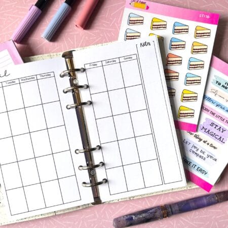 A personal ring planner open on a table. The top sheet shows a 'future log' insert. Around the planner are sticker sheets, a pink memo pad and some pens.