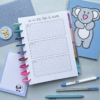 The Goal Setting Pages 10 set includes a goal tracker notebook with three labelled sections, coloured tabs, pens, a blue notebook featuring a cartoon koala, a sheep notepad, ruler, and planner sheets displayed on a light surface.