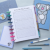 The "Goal Setting Pages 8" planner with a squared layout titled "Set the goal, make the change" is open on a desk, surrounded by animal-themed notebooks, pens, a sheep notepad, and a ruler.