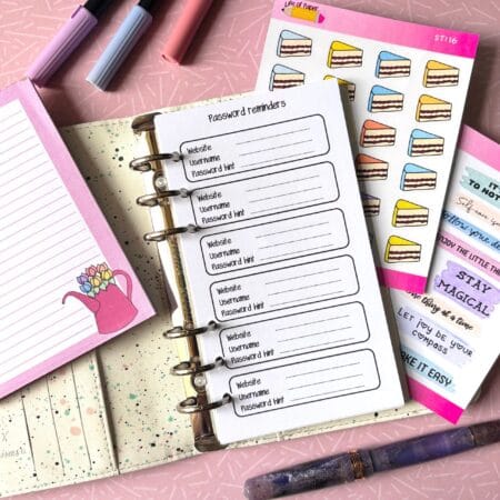 Password Reminder Personal Ring Insert A personal ring planner open on a table. The top sheet shows a 'password reminder' insert. Around the planner are sticker sheets, a pink memo pad and some pens.