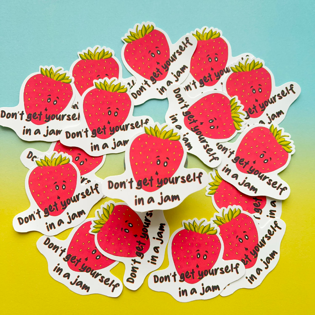Stickers all with the same design are scattered all over the image with one raised slightly in the centre. A strawberry with a happy face and underneath the text 'don't get yourself in a jam'. The image has a blue to yellow hombre effect background.