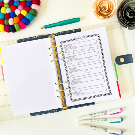 An open planner binder displays Snowball Debt Repayment Pages, surrounded by colourful pens, a green pen, and two paper flowers—ideal for managing your debt repayment plan on a felt ball coaster atop a white surface.