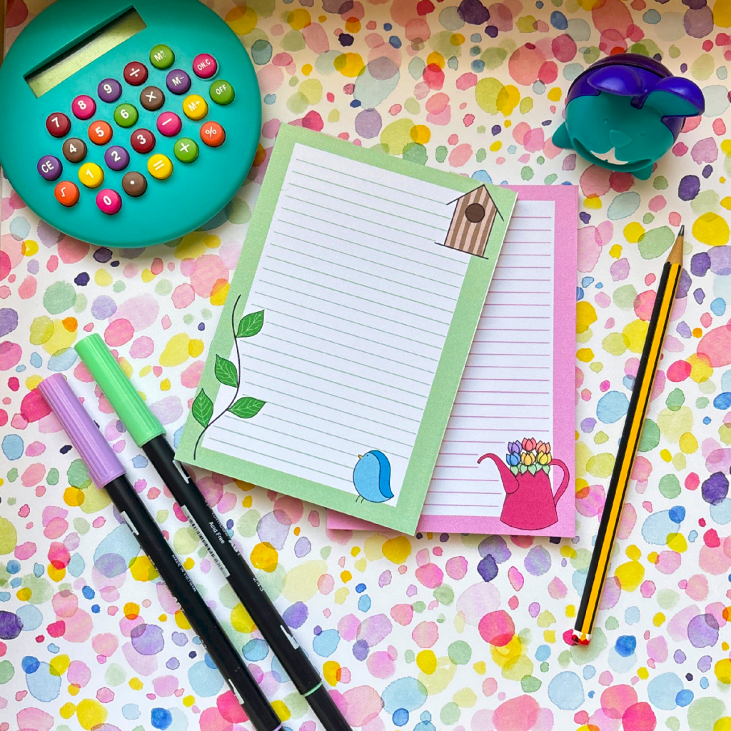 The Spring A6 Memo Pads Collection 2 includes two nature-themed memo pads, a teal calculator, a purple tape dispenser, two markers, and a pencil, all set on a vibrant polka-dotted background.
