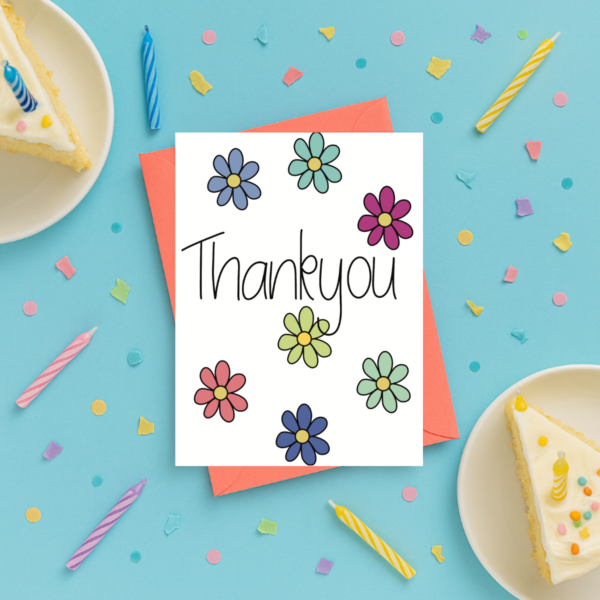 The Thank You Flowers Card rests on a coral envelope, with confetti, birthday candles, and two plates of cake slices arranged nearby on a light blue background.