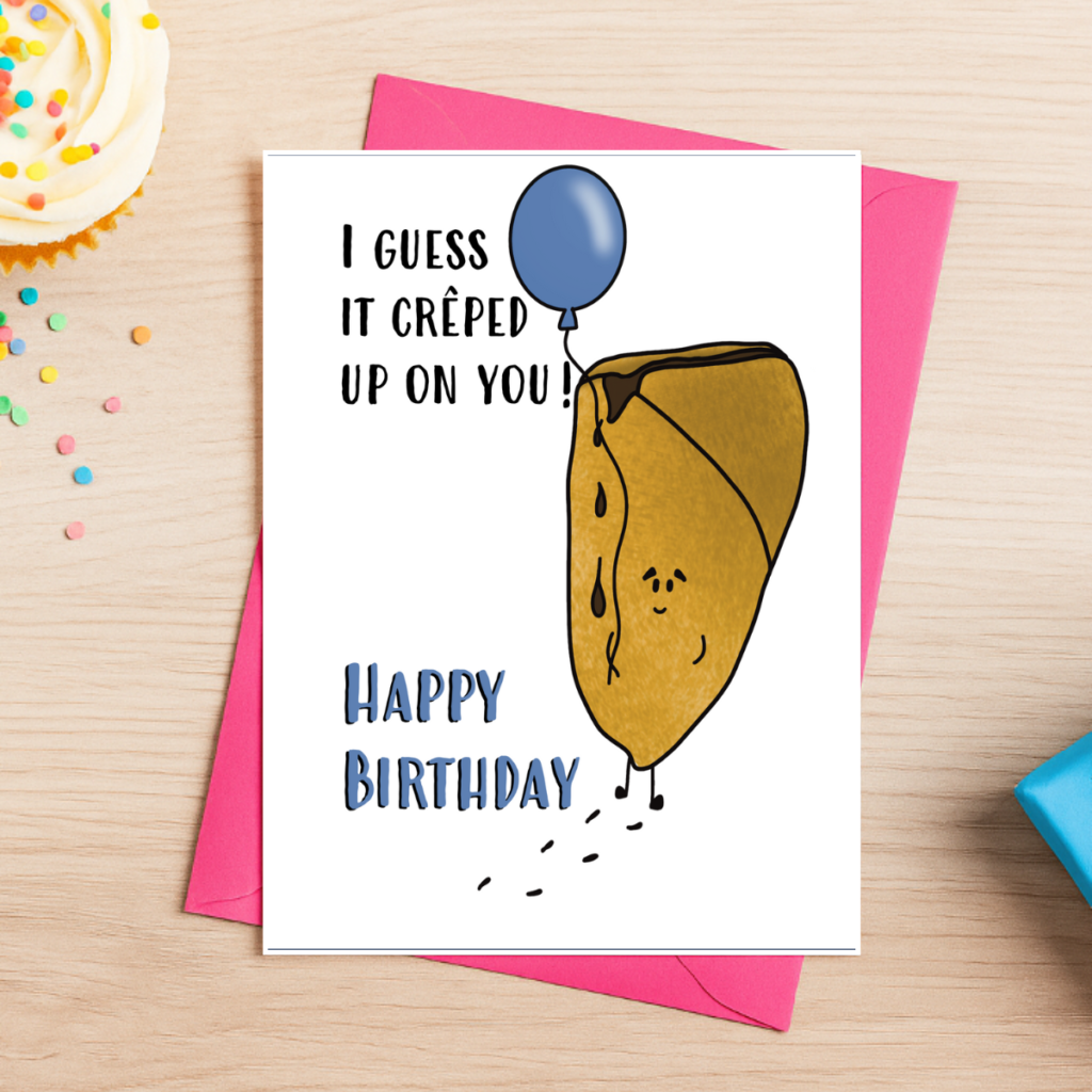 The Yummy Crêpe Birthday Card 4 features a cartoon crêpe with a blue balloon on a pink envelope, captioned "I guess it crêped up on you! Happy Birthday," with cupcake and confetti details on a wooden table.