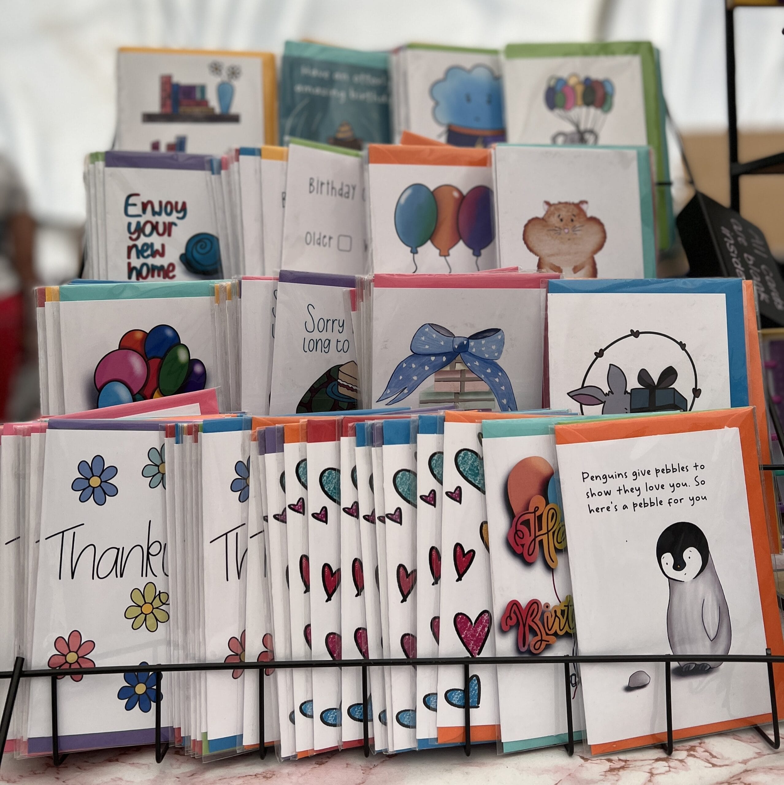 A tiered card stand in black with rows of greeting cards stood up on display.